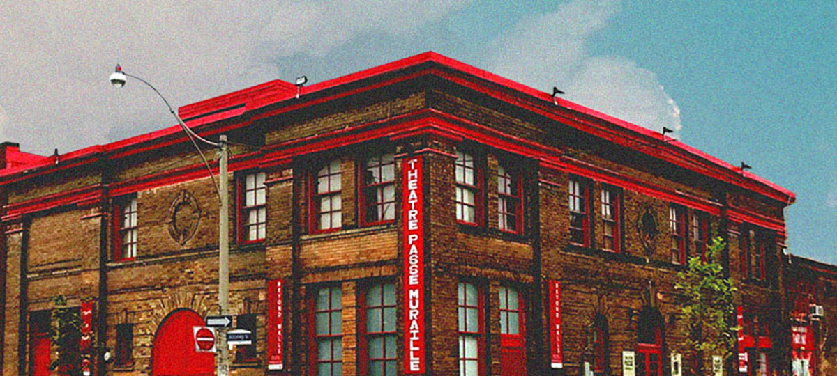 A vibrant image of theatre passe muraille building against sky with a big cloud. The building is made of bricks, and have red linings and a red door. Red banner in the front reads Theatre Passe Muraille