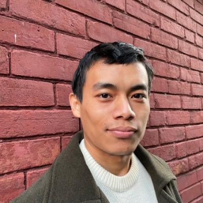 Graphic shows Norbu, a Himalayan man, smiling at the camera. He has black short hair and is standing in front of a red brick wall.