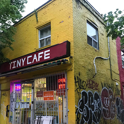 Tiny Cafe has a red sign on a Yellow brick building
